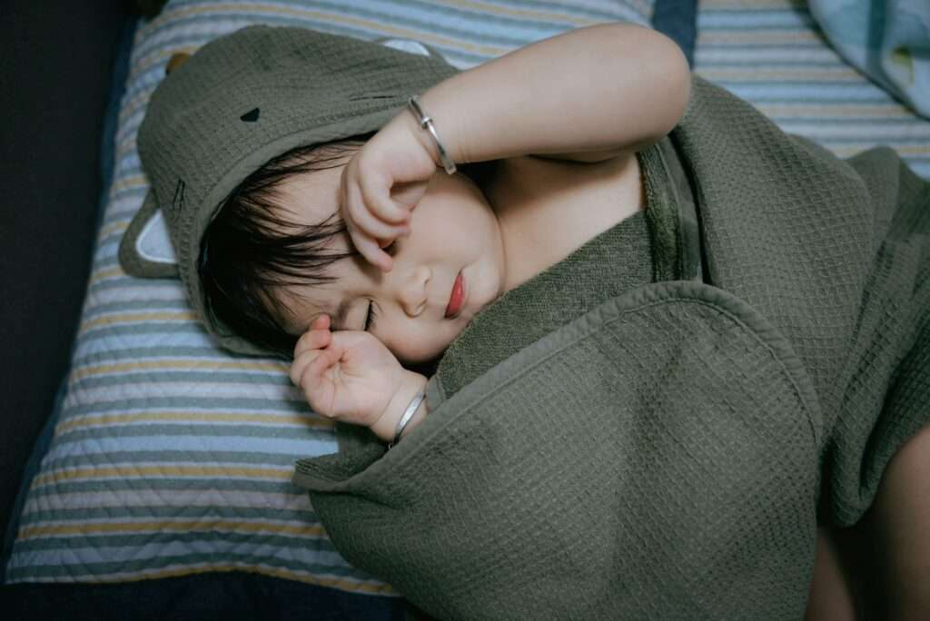 Nouveau-né endormi grâce à la technique de l'emmaillotage avec un grand lange bio.